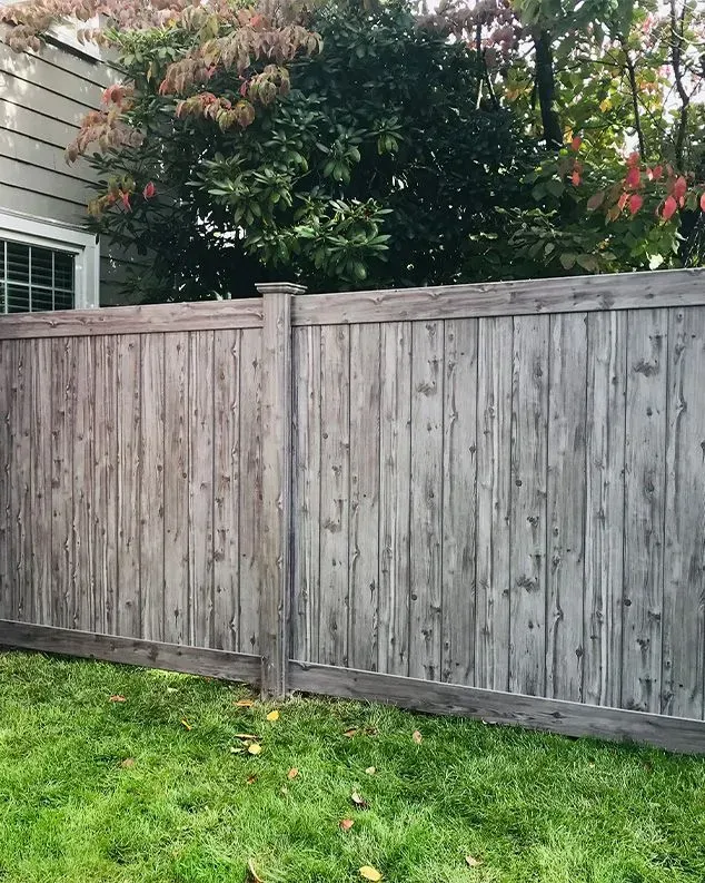 Weathered wooden fence with green grass and trees in the background.