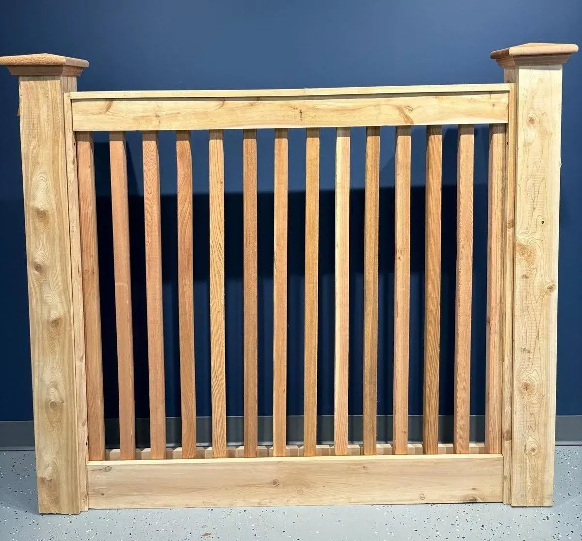 Wooden gate with vertical slats, light brown wood, against a blue wall.