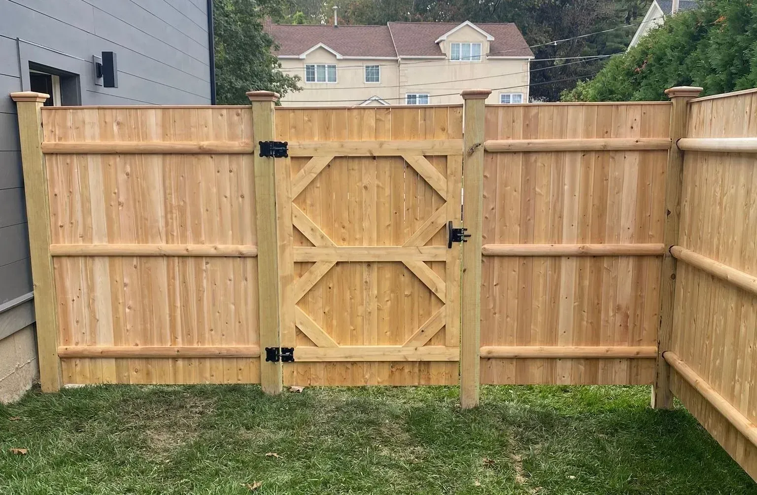 Wooden gate in a cedar fence, opening to a grassy yard. A house is visible in the background.