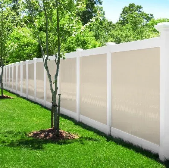 Gray and white vinyl fence in front of a white house with a green lawn and trees.