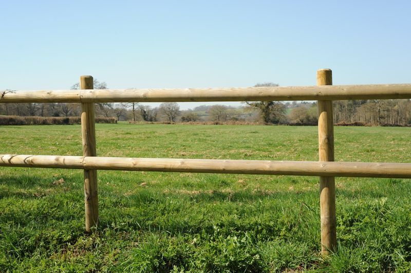 Wooden rail fence in a green field under a clear blue sky.