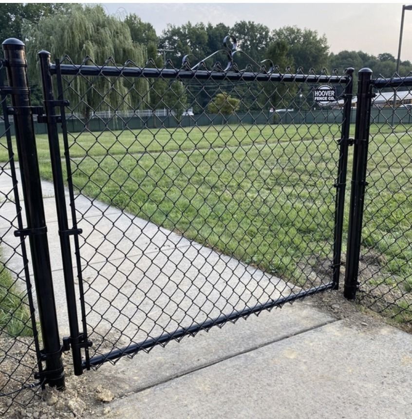 Black chain-link fence with a gate on a concrete path leading into a grassy area.